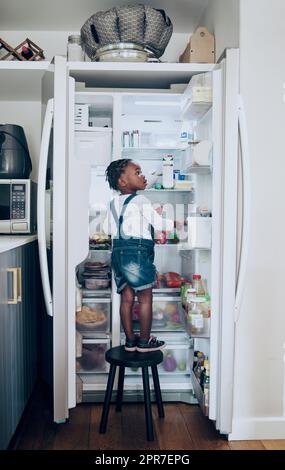 Snack-Zeit. Aufnahme eines Kleinkindes, das zu Hause Lebensmittel aus dem Kühlschrank nimmt. Stockfoto