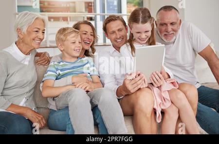 Glückliche Familie mit einem digitalen Tablet im Wohnzimmer zu Hause. Süßes kleines Mädchen und Junge, die sich mit Eltern und Großeltern in der Lounge verbinden. Einen Film ansehen und Technologie für Videoanrufe nutzen Stockfoto