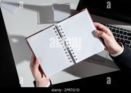 Geschäftsfrau, Die Ein Notizbuch Mit Neuen Ideen Über Dem Schreibtisch Mit Notizen Und Laptops In Der Hand Hat. Frau Im Anzug Mit Notizblock Mit Wichtigen Nachrichten Über Dem Tisch Mit Memos Und Computer. Stockfoto