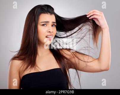 Warum ist es so verknotet. Studioportrait einer attraktiven jungen Frau, die einen Tag mit schlechten Haaren vor grauem Hintergrund hat. Stockfoto