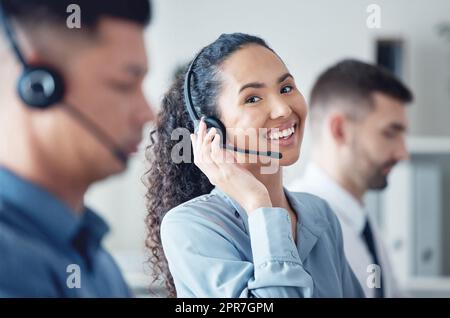 Ich kann Ihnen jederzeit helfen. Porträt einer jungen Callcenter-Agentin, die zusammen mit ihren Kollegen in einem Büro arbeitet. Stockfoto