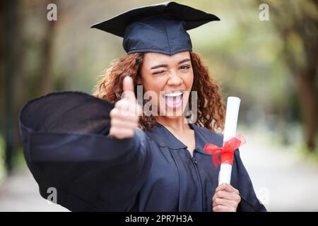 Möget ihr immer den Weg der Herrlichkeit gehen. Porträt einer jungen Frau, die ihr Diplom hält und am Abschlusstag den Daumen nach oben zeigt. Stockfoto