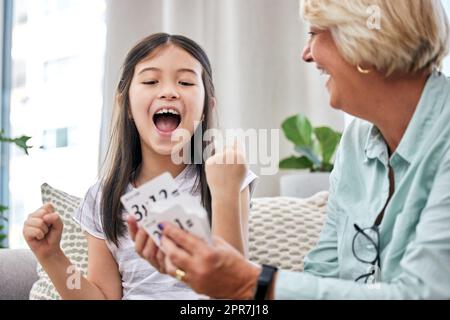 Ein kleines Mädchen und ihre Großmutter spielen zu Hause Karten. Stockfoto