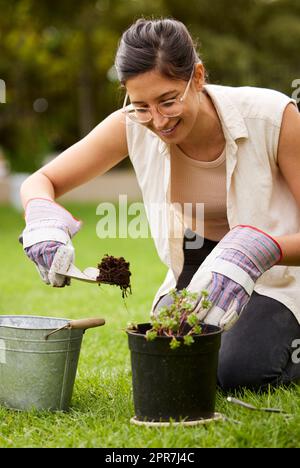 Gepflastert mit mehr als guten Absichten. Eine attraktive junge Frau, die mit einer Kelle grabt, während sie zu Hause etwas Gartenarbeit macht. Stockfoto