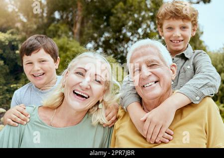 Porträt von zwei kleinen Jungen, die draußen Zeit mit ihren Großeltern verbringen. Reifes weißes Paar, das am Wochenende auf seine Enkel aufpasst und im Garten Spaß hat Stockfoto