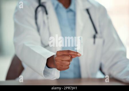 Hände eines Arztes, der einen Covid-Test hält. Nahaufnahme eines afroamerikanischen Arztes mit negativem Corona-Virus-Test. Mediziner, die mit einem Corona-Test an ihrem Schreibtisch sitzen. Stockfoto