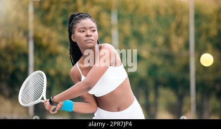 Junge Frau, die darauf wartet, einen Ball in einem Tennisspiel zu schlagen. Eine afroamerikanische Frau, die Tennis spielt. Eine seriöse junge Frau, die Tennis auf ihrem Club-Platz spielt. Aktiver, fitter Spieler, der einen Tennisball schlägt Stockfoto