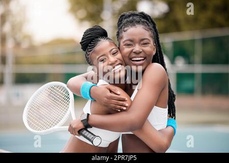 Porträt von zwei Freunden, die sich nach einem Match umarmen. Fröhliche junge Mädchen, die sich nach einem Tennisspiel umarmen. afroamerikanische Frauen, die nach einem Tennisspiel liebevoll sind. Glückliche Freunde auf einem Tennisplatz Stockfoto