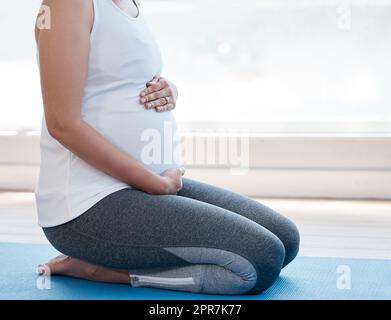 Ich kann es kaum erwarten, Euch zu treffen, eine Schwangere, die zu Hause Yoga macht. Stockfoto