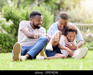 Eine Mutter und ein Vater kitzeln ihren Sohn, während sie sich im Freien entspannen. Stockfoto