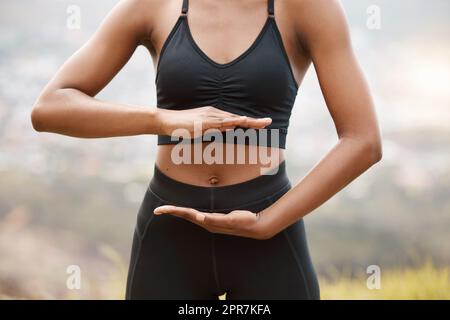 Eine afroamerikanische Frau, die ihren Bauch mit den Händen umrahmt, während sie draußen in der Natur steht. Engagierte schwarze Frau trainiert und trainiert im Freien, um ihre Gesundheit und Fitness zu verbessern Stockfoto