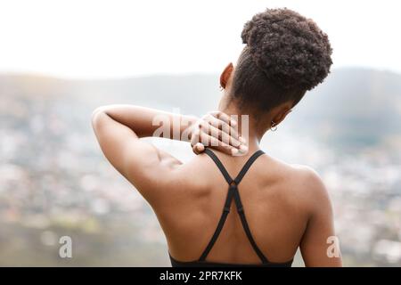 Aktive Frau, die ihren Nacken vor Schmerzen hält, während sie draußen trainiert. Nahaufnahme eines Athleten von hinten mit einer schmerzhaften Körperverletzung, die Unbehagen und Belastungen verursacht. Muskelverstauchung aus gebrochenen Gelenken Stockfoto