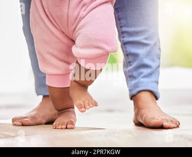 Tiefer Nahaufnahme eines Elternteils aus einer gemischten Rasse und der kleinen Babytöchter, die zu Hause zusammen auf dem Boden stehen. Mutter, die ihrem kleinen Baby das Laufen beibringt. Das Kind lernt, seine ersten Schritte zu Unternehmen Stockfoto