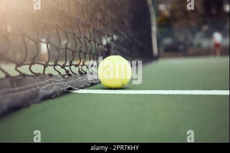 Nahaufnahme eines gelben Tennisballs auf dem Boden, nachdem er während eines Spiels auf einem Platz ein Netz getroffen hat. Still-Life-Ball in einer Reihe während eines Wettkampfsports in einem Sportverein. Verlieren durch Berühren des Netzes Stockfoto