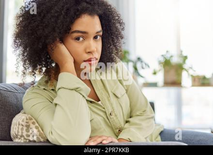 Junge Mischrasse, die allein zu Hause auf der Couch sitzt. Eine unglückliche hispanische Frau, die sich zu Hause langweilt. Eine Frau mit einem geschwungenen Afro, die zu Hause in der Lounge schmollt Stockfoto