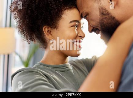 Glückliches gemischtes Paar, das sich zu Hause umarmt. Sorgenfreier hispanischer Ehemann und Ehefrau, die lächeln, während sie sich liebevoll in die Augen starren und sich zu Hause in der Lounge umarmen Stockfoto