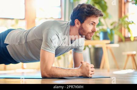 Ein passender junger weißer Mann, der Ellenbogen-Plank macht, hält das Körpergewicht beim Training zu Hause. Fokussierter Kerl fordert sich selbst heraus, Muskeln zu gewinnen, Oberkörper, Kernkraft zu verbessern und die Ausdauer beim Workout zu erhöhen Stockfoto