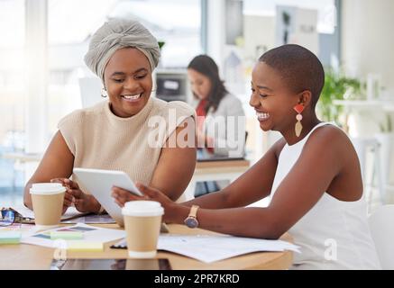 Lächelnde afroamerikanische Geschäftsfrauen sitzen zusammen und verwenden ein digitales Tablet während eines Brainstormings im Büro. Zuversichtlich glückliche schwarze Profis, die eine Strategie mit Technologie planen Stockfoto
