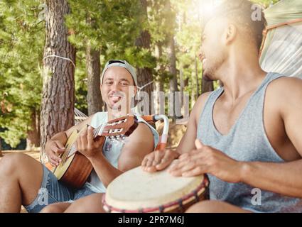 Musik machen im Wald. Zwei junge Männer sitzen und spielen Musikinstrumente während eines Campingausflugs im Wald. Stockfoto