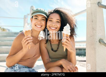 Darum geht es im Sommer. Verkürztes Porträt zweier attraktiver junger Freundinnen, die am Strand Eis genießen. Stockfoto