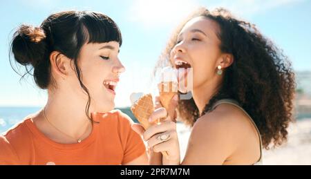 Die Jahreszeit des Sonnenscheins und des Lächelns. Zwei attraktive junge Freundinnen genießen Eis am Strand. Stockfoto