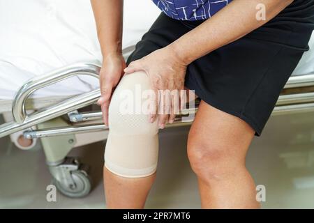 Asiatische ältere Frau trägt elastische Stützkniestütze zur Schmerzlinderung. Stockfoto
