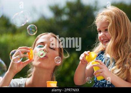 Lebenslange Erinnerungen zusammenbringen. Aufnahme einer jungen Mutter, die mit ihrer Tochter Blasen bläst. Stockfoto