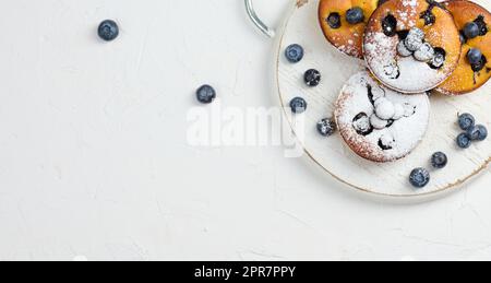 Runde Mini-Hüttenkäsepastete mit Blaubeeren auf einem weißen Holzbrett Stockfoto