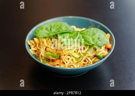 Spaghetti mit Gemüse und Basilikumblättern auf türkisfarbener Platte, Nahaufnahme Stockfoto