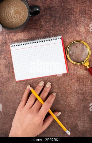 Frau Mit Spiralnotizbuch Mit Kopierfeld, Bleistift, Vergrößerungsglas Und Kaffeetasse Über Dem Tisch. Geschäftsfrau, Die Mit Einem Getränk Eine Wichtige Nachricht Auf Buch Schreibt. Stockfoto