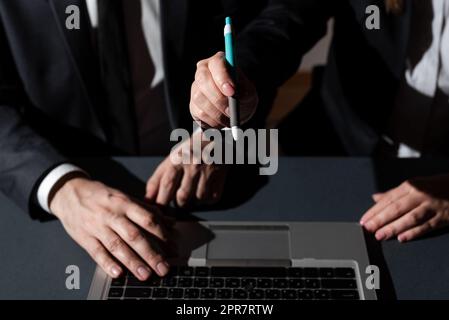 Ein Mann Tippt Auf Dem Laptop Und Eine Frau Zeigt Mit Dem Stift Auf Eine Wichtige Nachricht. Ein Geschäftsmann, Der Über Computer Schreibt, Und Eine Geschäftsfrau, Die Grausame Informationen Präsentiert. Stockfoto