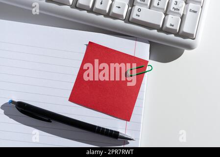 Haftnotiz Mit Wichtiger Nachricht Auf Geöffnetem Notizbuch Am Schreibtisch Mit Stift Und Tastatur. Grundlegende Informationen In Einem Memo Im Notizblock Neben Dem Bleistift. Stockfoto