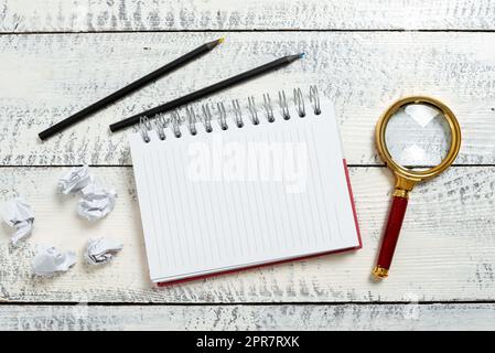 Notizbuch Mit Wichtigen Mitteilungen Auf Dem Boden Mit Papierfolien, Lupe Und Bleistiften. Notizblock Mit Neuen Ideen Mit Zerknitterten Notizen, Vergrößerungsglas Und Buntstiften Überall. Stockfoto