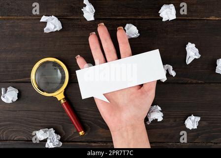 Hand Einer Geschäftsfrau Mit Think Bubble Sheet Und Lupe, Umgeben Von Zerknitterten Papieren Über Dem Tisch. Holding Sheet Für Frauen Mit Werbetexten Für Business-Branding. Stockfoto