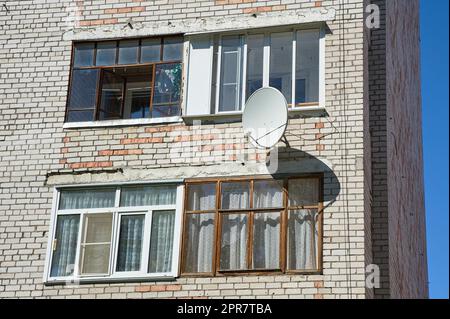 Eine Satellitenschüssel hängt an der Wand eines Backsteinhauses Stockfoto