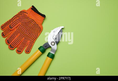 Große Gartenschere zum Schneiden von Ästen an Bäumen und orangefarbene Textilhandschuhe Stockfoto