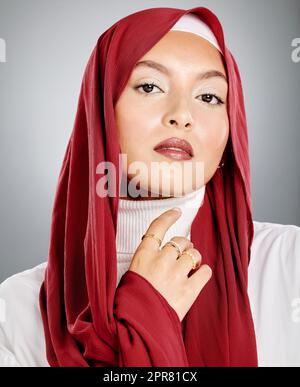 Porträt einer muslimischen Frau, die einen roten Hijab oder Kopftuch trägt und ihre Wimpern und Make-up zeigt. Ihre makellose Haut glüht. Schöne Frau isoliert vor grauem Studiohintergrund. Stockfoto