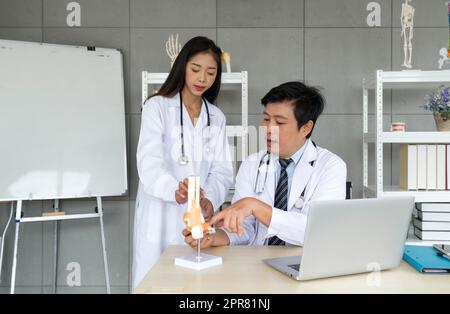 Junge asiatische Orthopädische Chirurgen in weißem Kleid und Stethoskop, die den Professor um Rat zu Knochen, Gelenk, Sehne und Muskel bitten. Arbeitsatmosphäre im Krankenhaus. Stockfoto