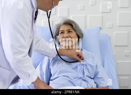 Ältere Patientin und Ärztin. Der asiatische Arzt verwendet ein Stethoskop, um den Herzschlag des älteren Patienten zu überprüfen. Stockfoto