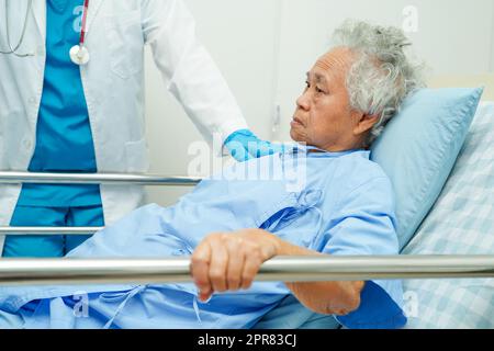 Ältere ältere Patientin aus Asien, die mit einem Bettlageschiene in der Hand lag, während sie mit Hoffnung ihre Familie im Krankenhaus erwartete. Stockfoto