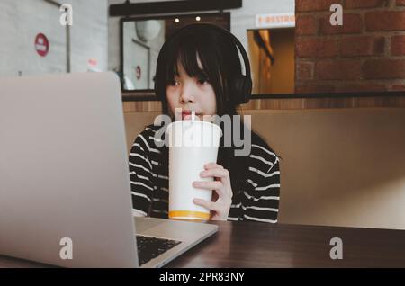 Mädchen im Teenageralter, die Kopfhörer tragen, schauen sich Filme an, spielen Social Media oder lernen online, indem sie Wasser trinken und sich auf dem Sofa entspannen. Stockfoto