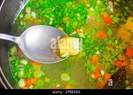 Esslöffel mit einer Scheibe gekochte Kartoffeln aus Gemüsesuppe mit Kräutern. Koch zu Hause Stockfoto