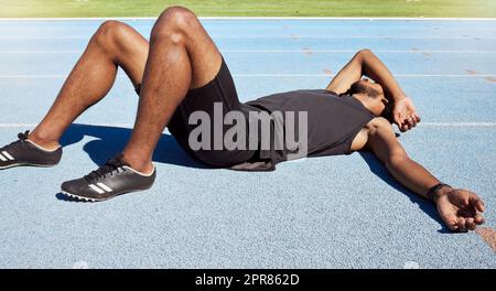 Nahaufnahme eines fit aktiven jungen männlichen Athleten, der nach einem Rennen flach auf der Strecke liegt und sich nach einem Sprint auf einer Laufstrecke müde fühlt. Männchen mangelte es nach einem harten Trainingslauf an Energie Stockfoto