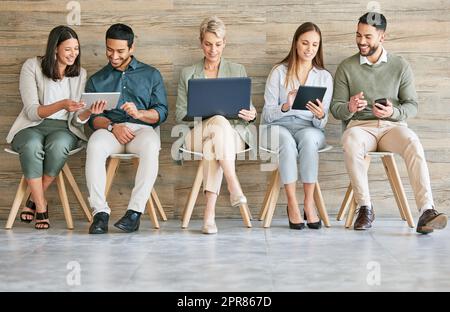 Ohne Technologie könnte es kein Geschäft geben. In voller Länge eine vielfältige Gruppe von Geschäftsleuten, die in einer Reihe zusammen sitzen und Technologie einsetzen. Stockfoto