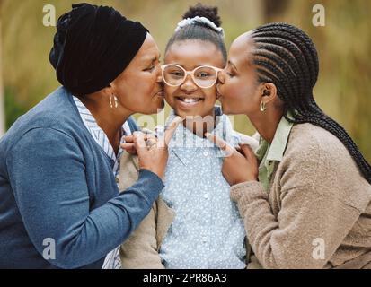 So viel Liebe auf einem Bild. Beschnittenes Porträt eines entzückenden kleinen Mädchens, das von ihrer Mutter und Großmutter auf die Wangen geküsst wird. Stockfoto