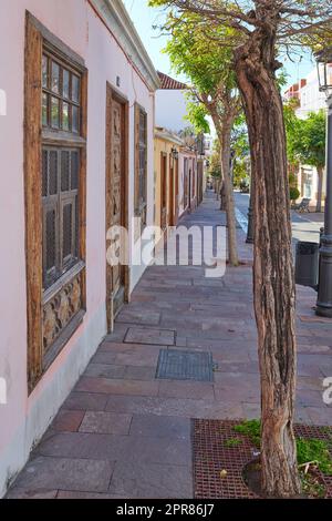 Stadtblick, gepflasterter Bürgersteig mit Bäumen und Wohnhäusern oder Gebäuden in einer ruhigen Straße in Santa Cruz, La Palma, Spanien. Historische spanische und koloniale Architektur und berühmtes Reiseziel Stockfoto