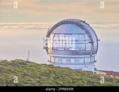 Nahaufnahme eines astronomischen Observatoriums mit klarem Himmel und Kopierraum. Das Teleskop ist von Grün umgeben und befindet sich auf einer Insel am Rand einer Klippe. Roque de los Muchachos Observatorium in La Palma Stockfoto