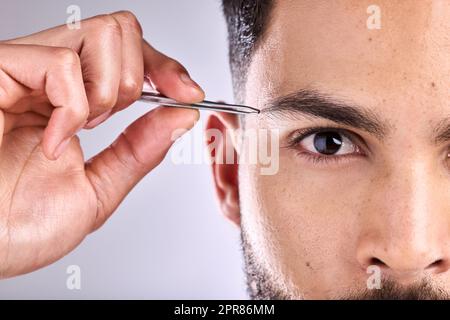 Sie sind fast perfekt. Nahaufnahme eines jungen Mannes, der seine Augenbrauen vor grauem Hintergrund zupft. Stockfoto