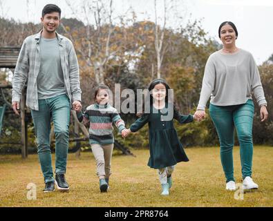 Wir sorgen dafür, dass es Zeit für die Familienbindung gibt. Ganzkörperaufnahme einer jungen Familie, die sich die Hände hält und durch den Park geht. Stockfoto