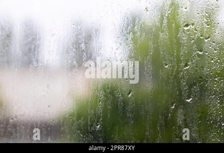 Starker Regen. Regentropfen auf dem Fensterglas an einem Sommertag. Selektiver Fokus, geringe Tiefenschärfe. Wassertropfen fallen auf ein nasses Fenster. Ein Glas voll Stockfoto